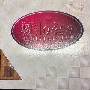 May include: A box with the text "Noëse Collection" in a red oval with a silver border. The box has a chess piece and a geometric pattern. The text is in a stylized font.