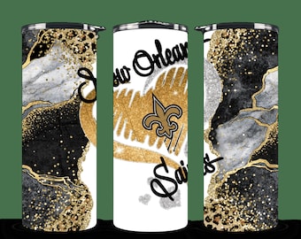 May include: Three stainless steel tumblers with a black, white, and gold marble design. The center tumbler features the New Orleans Saints logo and the text "New Orleans Saints".