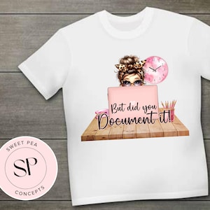 Peut inclure: T-shirt blanc avec un motif d'une femme portant des lunettes et un bandeau léopard, travaillant sur un ordinateur portable rose. Le texte "But did you Document it!" est affiché sur l'ordinateur portable. Une horloge rose et des crayons sont également présents.