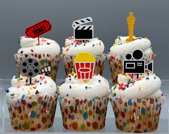 May include: Six decorated cupcakes with various movie-themed toppers. The cupcakes are topped with colorful sprinkles and have a white frosting base. The toppers include a film reel, a movie clapperboard, a popcorn bucket, a golden statue, and a video camera.