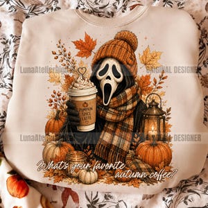 May include: A cream-colored sweatshirt featuring a graphic of a ghost character wearing an orange knit beanie and plaid scarf, holding a Pumpkin Spice Latte cup. The design includes pumpkins, autumn leaves, a lantern, and the text What's your favorite autumn coffee?