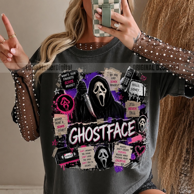 May include: A charcoal gray t-shirt with long sheer sleeves embellished with white pearls. The front features a graphic print of the Ghostface character holding a knife, surrounded by movie-themed text, a VHS tape, and purple accents.