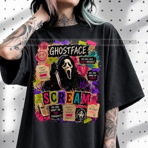 May include: A black t-shirt featuring a graphic print of the Ghostface character from the movie Scream. The design includes colorful paint splatters, a telephone, hearts, and text quotes such as Do You Like Scary Movies and What's Your Favorite Scary Movie.