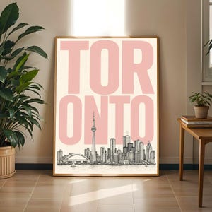 Könnte beinhalten: Ein rechteckiger Wandkunstdruck mit dem Wort TORONTO in großen, hellrosa Großbuchstaben, die über einer detaillierten schwarz-weißen Strichzeichnung der Skyline von Toronto, einschließlich des CN Towers, auf einem cremefarbenen Hintergrund liegen.