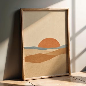 Könnte beinhalten: Ein gerahmter Kunstdruck mit einer stilisierten Landschaft, bestehend aus einer großen orangefarbenen Halbkreis-Sonne, einer dünnen blauen Horizontlinie sowie geschichteten sandfarbenen und braunen Dünen auf beigem Grund.