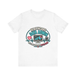 Może przedstawiać: Biały t-shirt z krótkim rękawem z grafiką zawierającą tekst HEALTHCARE DATA ADMIN oraz WE TURN DATA INTO BETTER CARE. Wzór przedstawia monitor komputerowy z wykresami, ikonę serca z linią EKG oraz ikonę podkładki z klipsem.