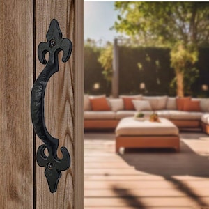 May include: Black metal door handle with a decorative fleur-de-lis design. The handle is mounted on a wooden door.