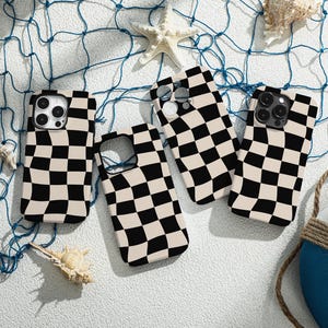 Puede incluir: Cuatro fundas de teléfono diferentes con un patrón a cuadros en blanco y negro. Las fundas están dispuestas sobre una superficie blanca con una red de pesca azul y un salvavidas.
