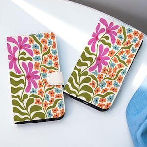 May include: Two phone cases with a floral pattern. The cases display a white backdrop adorned with pink flowers, orange and blue blooms, and green foliage. One case is open, while the other is closed with a white strap.