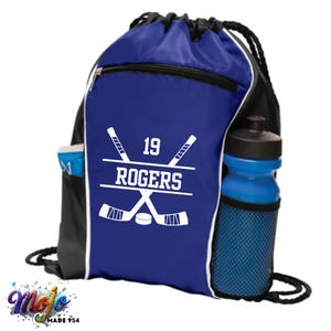 Könnte beinhalten: Blaue und schwarze Sporttasche mit Kordelzug und einem weißen Hockeyschläger-Design, der Nummer 19 und dem Namen "ROGERS".