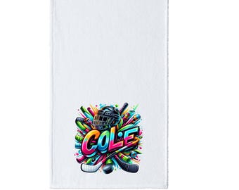 May include: White towel with a colorful graphic design featuring a hockey helmet, sticks, and the name "COLE" in vibrant, multi-colored letters. The design includes shades of green, blue, yellow, and red.