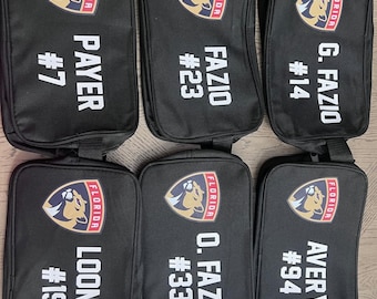 May include: Six black zippered bags with a Florida Panthers logo and player names and numbers. The bags are lined up in a row on a table.
