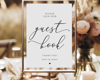 May include: A white sign with a black frame and stand, with the text "Please sign our guest book" and "Thank you! Kate & James" in black script font.