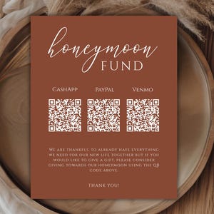 May include: A brown card with white text that reads "honeymoon fund". The card has three QR codes labeled "CashApp", "PayPal", and "Venmo". The text below the QR codes reads "We are thankful to already have everything we need for our new life together but if you would like to give a gift, please consider giving towards our honeymoon using the QR code above. Thank you!"