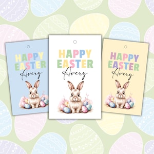 May include: Three Easter gift tags featuring a bunny holding colourful eggs. The tags are blue, white and yellow with the text "Happy Easter Avery" on each.
