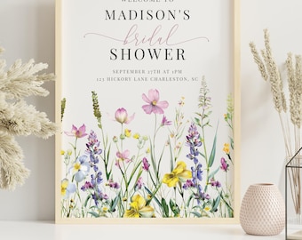 May include: A framed sign with the text "WELCOME TO MADISON'S bridal SHOWER" in a delicate script. The sign features a floral border with watercolor-style flowers in shades of pink, purple, and yellow. The date and location are also printed on the sign.