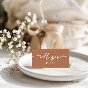 May include: A brown place card with white cursive text that reads "allison JONES".