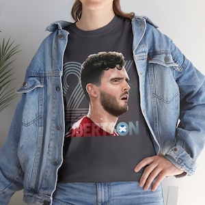 May include: Dark gray t-shirt featuring a portrait of a man with the name "ROBERTSON" and the number "22" in a retro design. The shirt also includes a Scottish flag emblem.