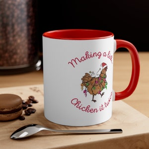 May include: White ceramic coffee mug with a red rim and handle. The mug features a cartoon chicken wearing a Santa hat and tangled in Christmas lights. The text "Making a list... Chicken it twice" is printed in red on the mug.