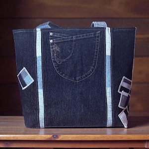 Peut inclure: Un sac fourre-tout en jean bleu foncé avec une poche et des patchs décoratifs. Le sac présente des rayures bleues claires et blanches sur les côtés et une poche en jean avec des coutures décoratives. Le sac a deux poignées.