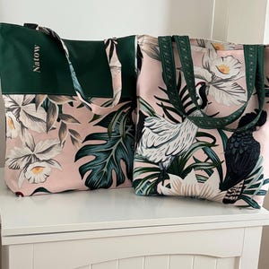 Peut inclure: Deux sacs cabas avec des motifs floraux roses et verts. Un sac a un panneau vert avec le mot "Natow" brodé dessus. Les deux sacs ont des anses vertes.
