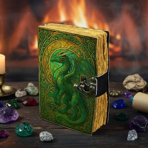 May include: A leather-bound journal with a green dragon design on the cover. The dragon is detailed with green and gold accents. The journal has a metal clasp and aged paper pages. The background includes a fireplace and scattered gemstones.