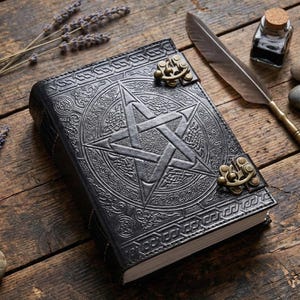 Puede incluir: Diario de cuero negro con un dise&ntilde;o de pentagrama en relieve y nudos celtas. El diario tiene un cierre de broche y est&aacute; sobre una superficie de madera con una pluma, tintero y ramitas de lavanda.