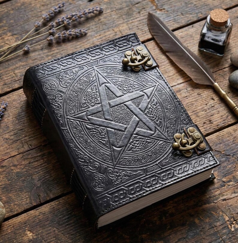 Puede incluir: Diario de cuero negro con un dise&ntilde;o de pentagrama en relieve y nudos celtas. El diario tiene un cierre de broche y est&aacute; sobre una superficie de madera con una pluma, tintero y ramitas de lavanda.