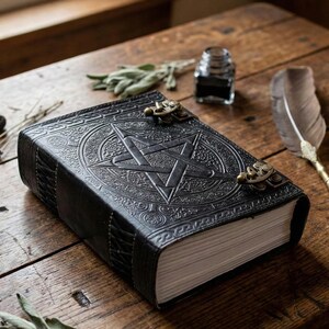 Puede incluir: Un diario de cuero negro con un dise&ntilde;o de pentagrama en relieve en la portada. El diario tiene cierres de lat&oacute;n y un borde decorativo. Las p&aacute;ginas son de color crema y el diario est&aacute; sobre una superficie de madera.