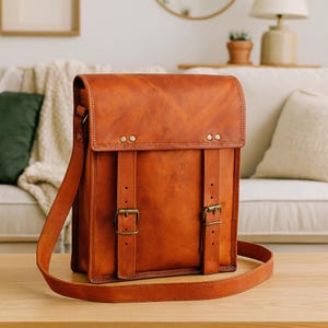 Könnte beinhalten: Eine braune Leder-Umhängetasche mit Klappenverschluss und verstellbarem Schulterriemen. Die Tasche hat zwei Schnallenverschlüsse und dekorative Nähte. Die Tasche ist rechteckig und scheint aus hochwertigem Leder zu sein.
