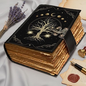 May include: A black journal with a celestial tree design and a metal clasp. The pages have a vintage, aged appearance. A leather strap secures the journal. A bundle of lavender and a wax seal are nearby.