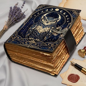 May include: A decorative journal with a blue cover featuring an owl design, moon phases, and stars. The journal has a black leather strap closure and aged-looking pages. A bundle of lavender and a wax seal are also visible.