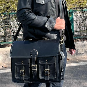 May include: Black leather messenger bag with two front pockets, brass buckles, and a top handle. The bag has a flap closure and a shoulder strap. The bag is carried over the shoulder.