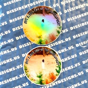 May include: Two circular stickers with the text "NOT A BIG FAN OF THE GOVERNMENT" in a circular design. One has a rainbow background, the other a landscape scene. They are on a blue background with white text.
