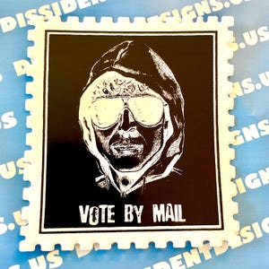 May include: A black and white sticker in the shape of a postage stamp. The sticker features a stylized image of a person wearing sunglasses and a hooded sweatshirt. The text "VOTE BY MAIL" is printed at the bottom.