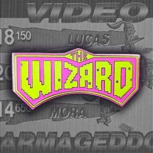 Könnte beinhalten: Eine rosa und grüne Emaille-Anstecknadel mit dem Text "THE WIZARD" in einer Pixel-Schriftart.