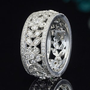 May include: A silver floral wedding band with a delicate design of leaves and flowers encrusted with small diamonds.