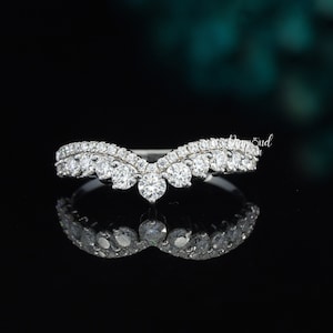 May include: A silver band ring with a V-shaped design featuring a row of small round clear stones on each side and a larger centre stone.