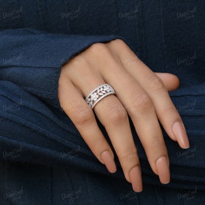 Pode incluir: Um anel de prata com um design floral cravejado com pequenos diamantes transparentes. O anel &eacute; usado no dedo m&eacute;dio de uma m&atilde;o com tom de pele claro.