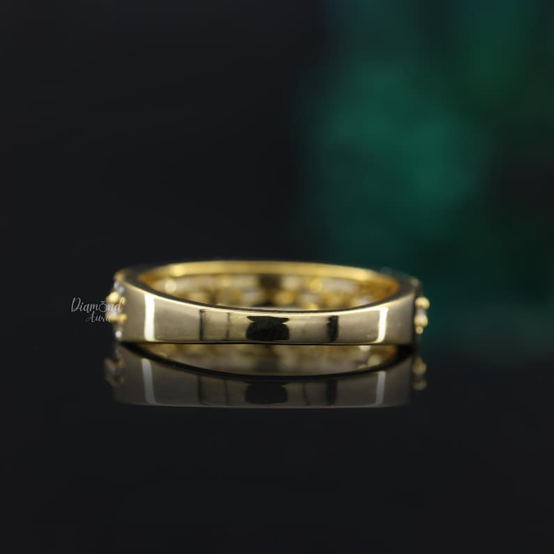 May include: A gold band ring with a row of small clear stones set in the band. The ring is shown from the side.