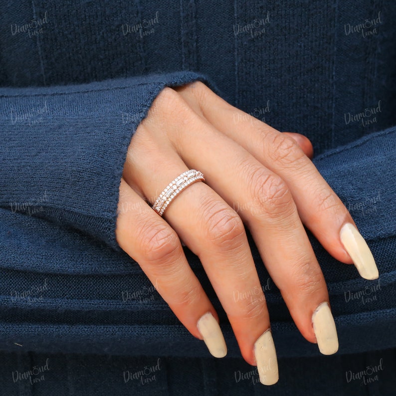 May include: A thin, delicate, silver band ring with multiple rows of small, clear, round diamonds. The ring is worn on the ring finger of a hand with light-colored nail polish.