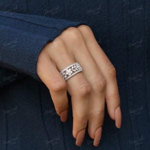 Pode incluir: Um anel de banda de prata com um design floral com pequenas pedras preciosas transparentes. O anel est&aacute; no dedo de uma pessoa.