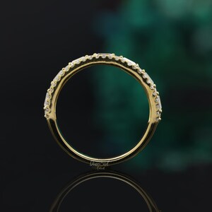 May include: A gold band with a row of small, clear, square-shaped diamonds set in the metal. The band is smooth and polished.