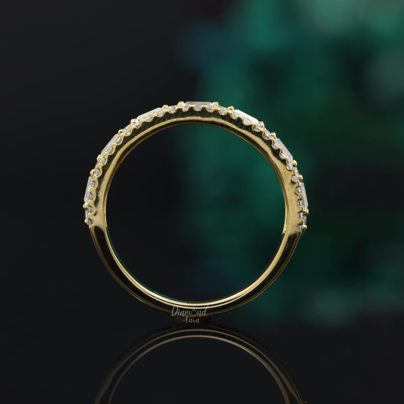 May include: A gold band with a row of small, clear, square-shaped diamonds set in the metal. The band is smooth and polished.