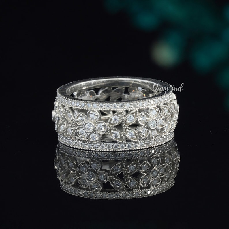 Pode incluir: Um anel de banda de prata com um design floral com pequenas pedras transparentes. O anel est&aacute; sobre um fundo preto.