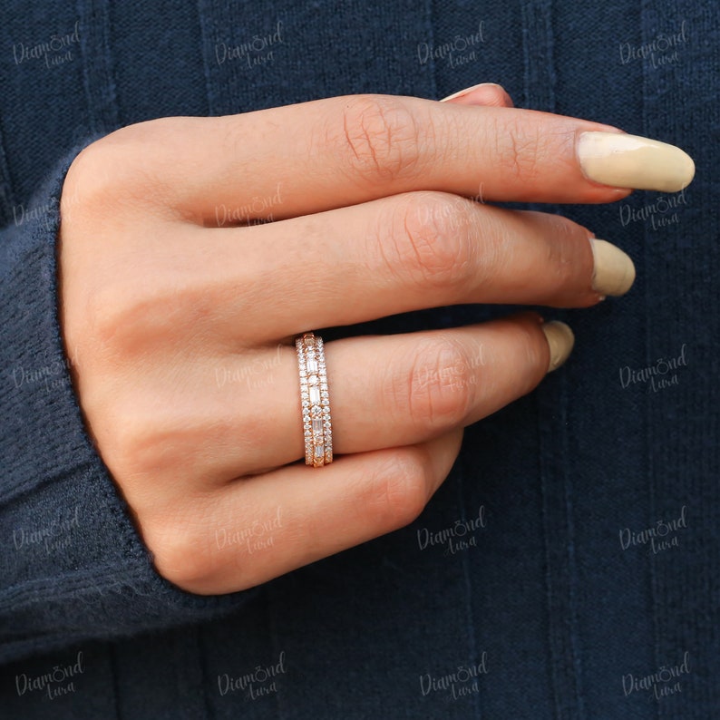 May include: A rose gold band ring with three rows of pave set diamonds. The ring is on a finger with light beige nail polish.