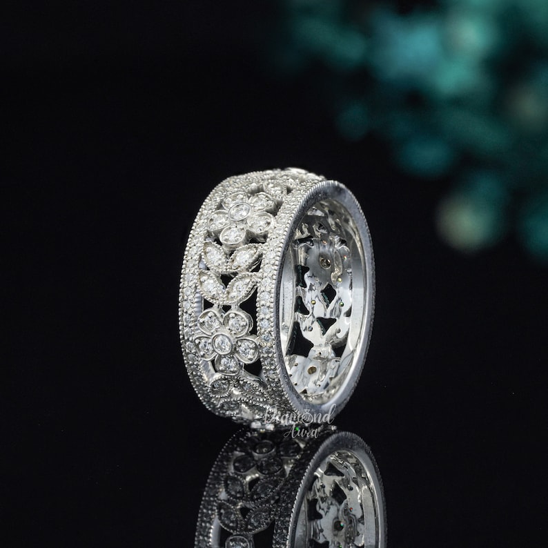 May include: A silver floral wedding band with a delicate design of leaves and flowers encrusted with small diamonds.