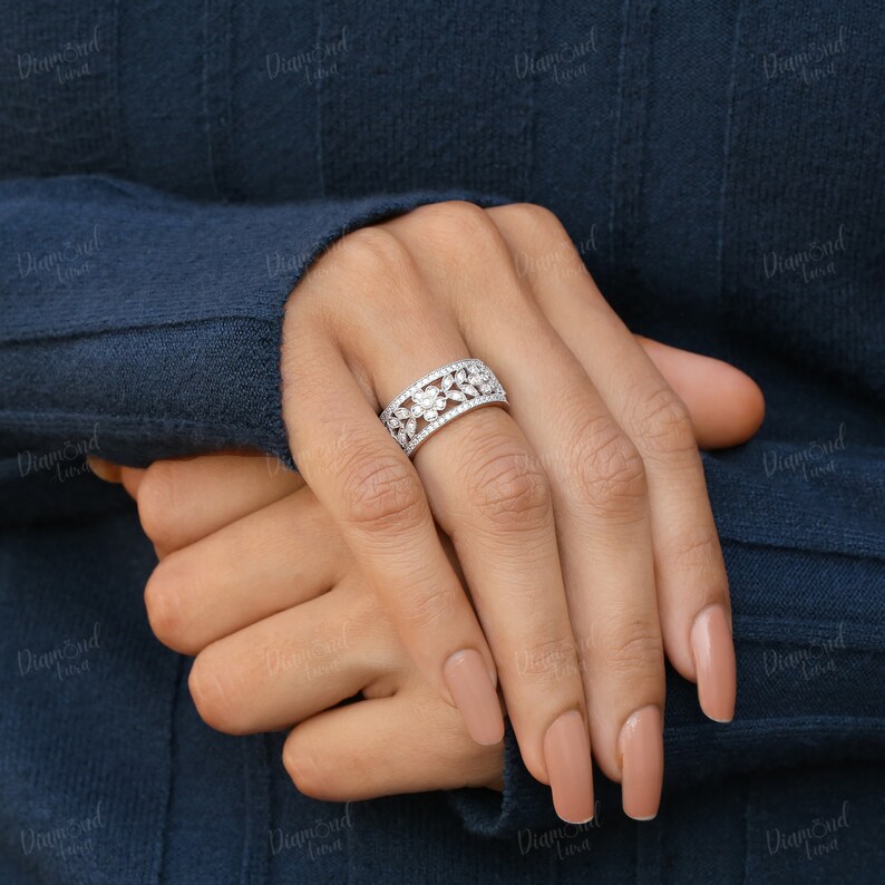 Pode incluir: Um anel de prata com um design floral cravejado com pequenos diamantes transparentes. O anel &eacute; usado no dedo anelar de uma m&atilde;o.