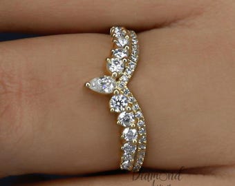 May include: A curved, gold-toned ring with a pear-shaped diamond and several round diamonds. The ring features a delicate design with multiple small, sparkling stones. The ring is set with a gold band and is designed to be worn on a finger.