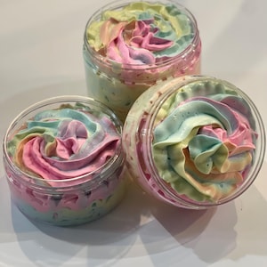 May include: Three jars of whipped body butter with a rainbow swirl design. The jars are clear plastic and the body butter is a light pink, yellow, and blue color.